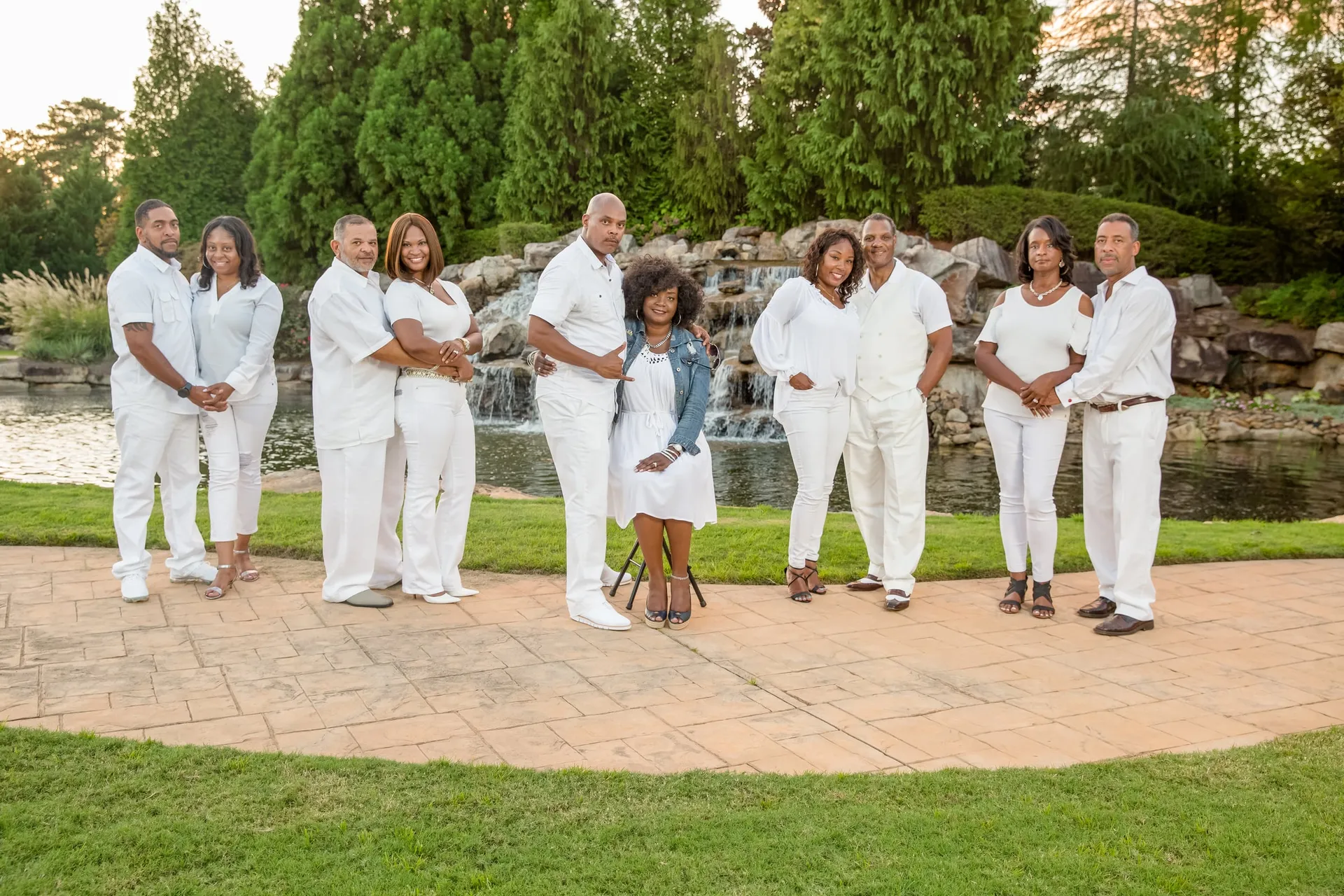 An extended family dressed in white gathered on a lawn before a rocky waterfall.
