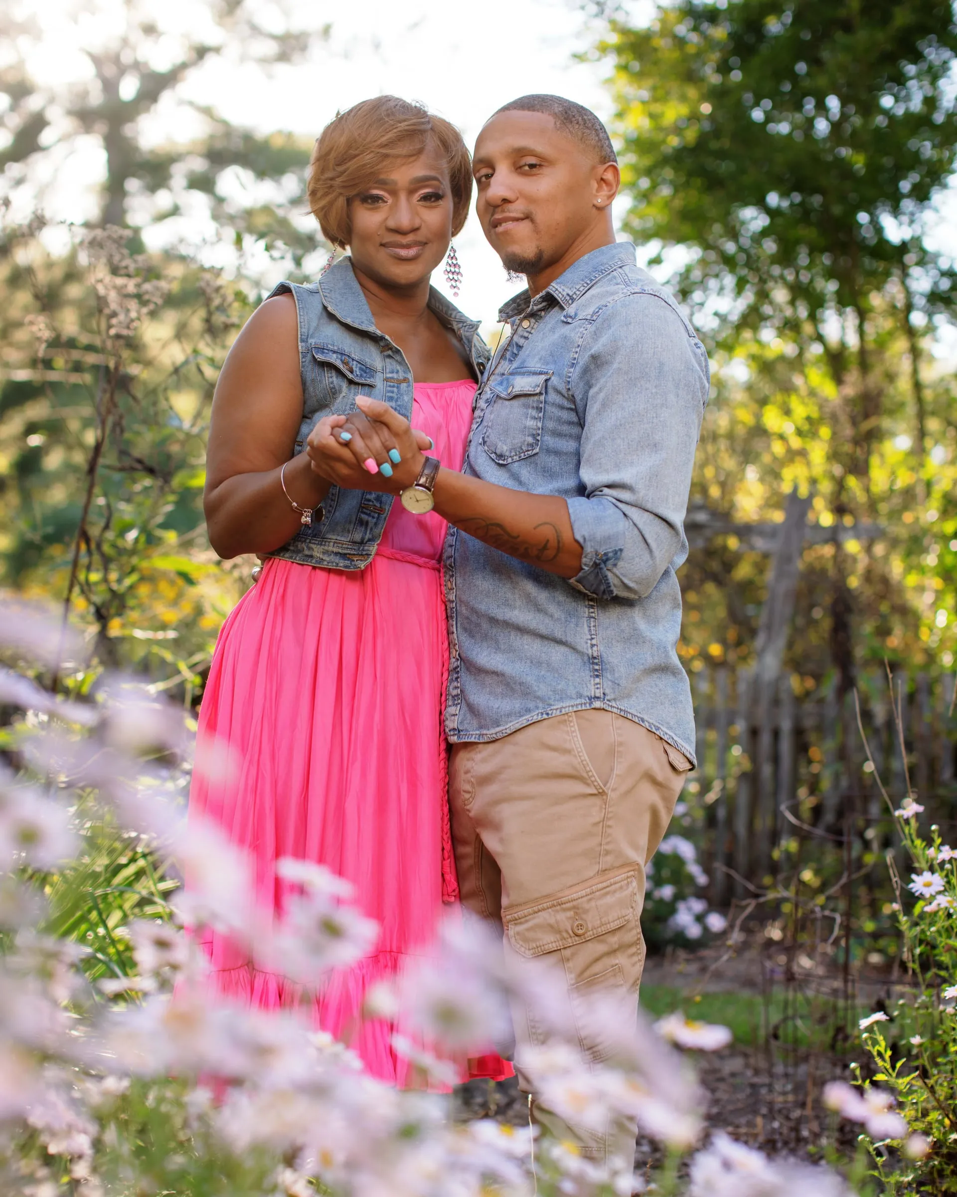A couple in denim and a pink skirt holding hands in a meadow of purple wildflowers.