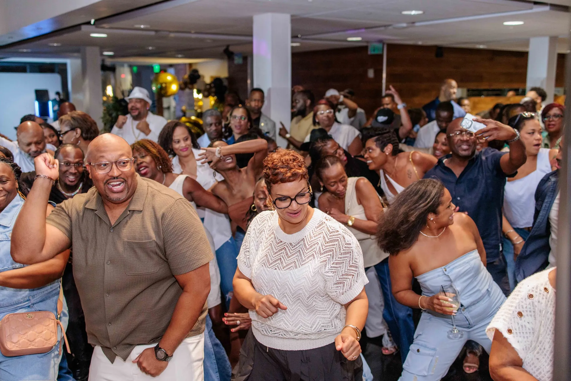 A packed dance floor of guests in white moving together at an all-white birthday party.