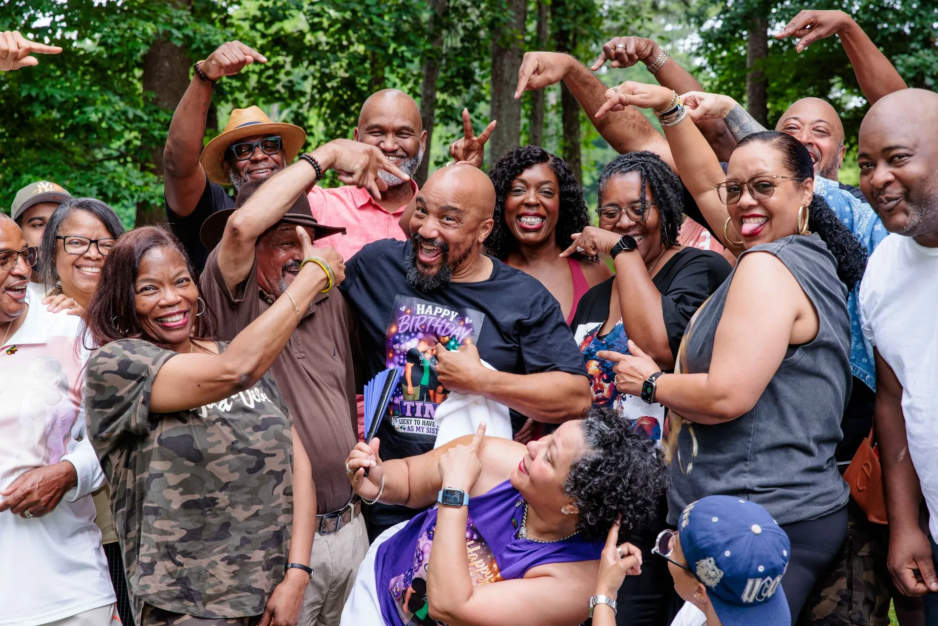 Family and friends pointing at the birthday honoree in the middle of an outdoor party crowd.