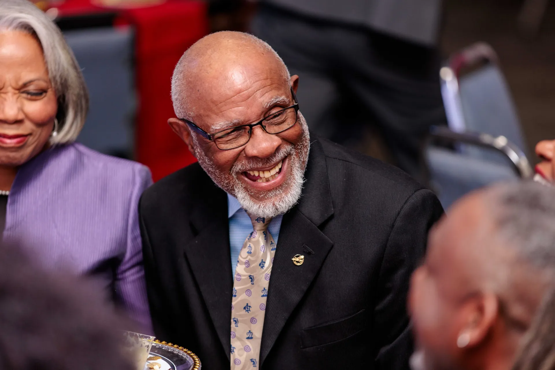 A guest in a navy suit and gold tie laughing at a company anniversary dinner.
