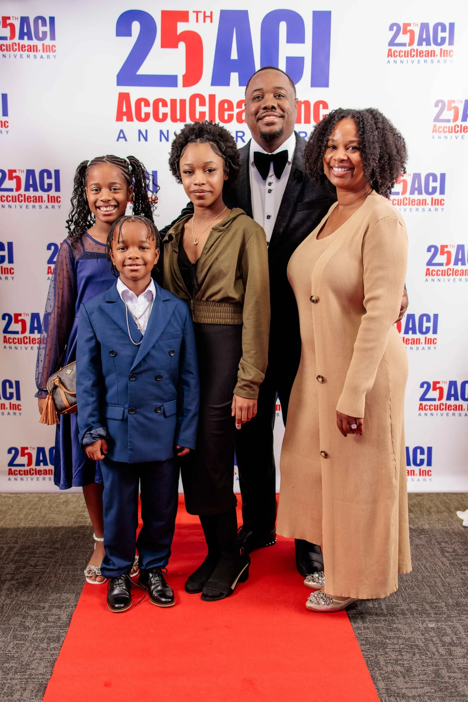 A family in evening wear posing on the red carpet before a company anniversary backdrop.