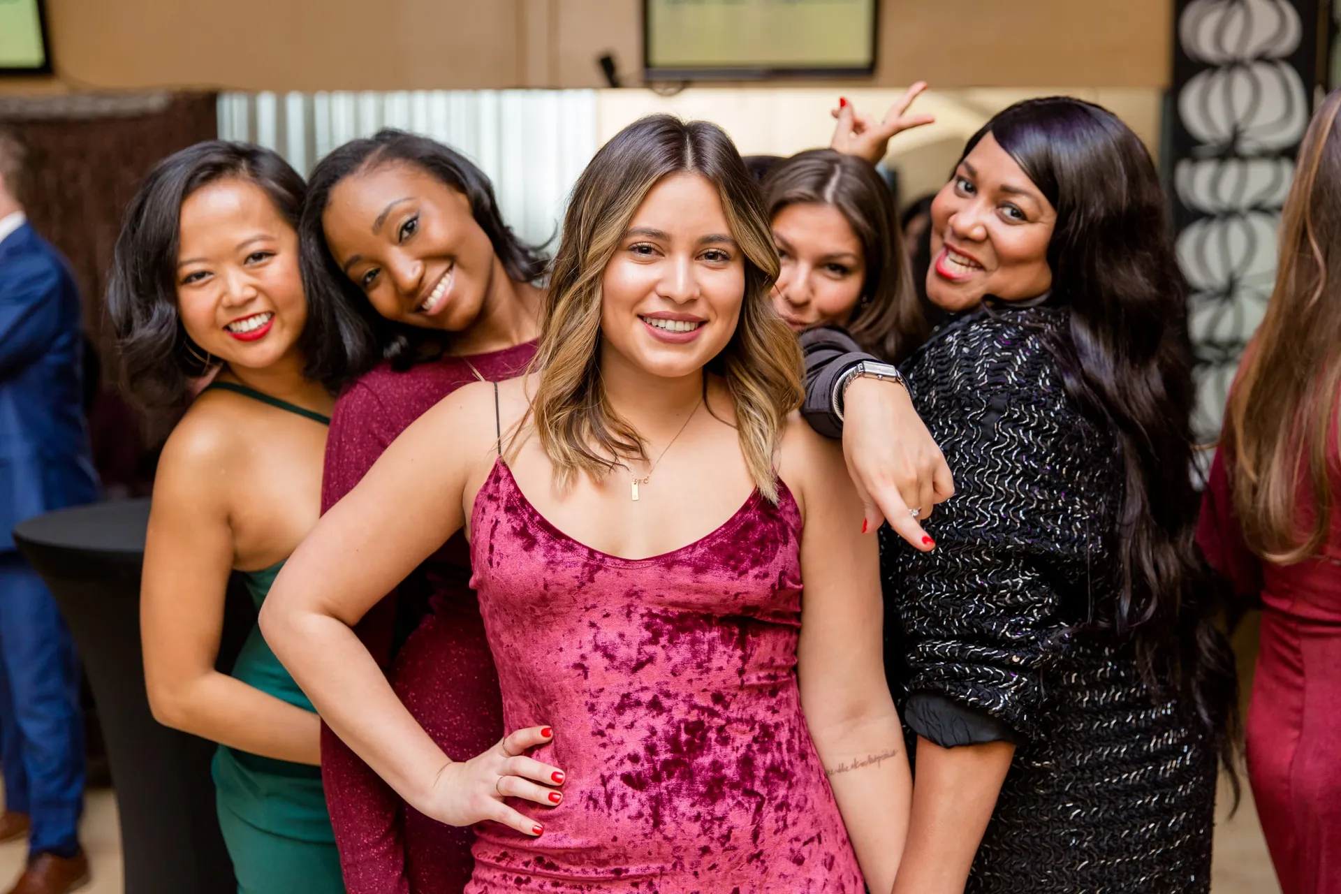 Five colleagues in party dresses posing together in a hotel lobby at a corporate event.