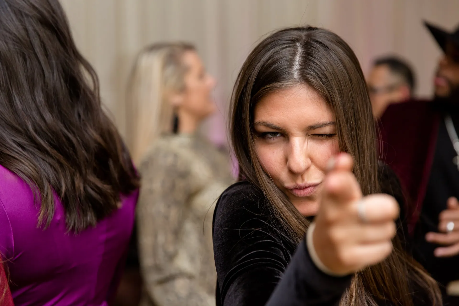 A guest winking and pointing at the camera on the floor of a corporate party.