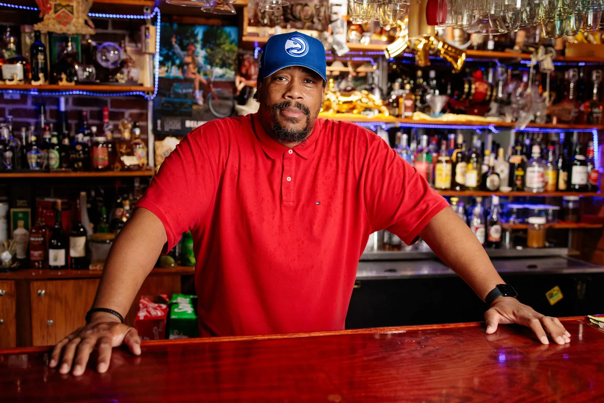 A guest in a red polo and ball cap leaning on a well-stocked bar.