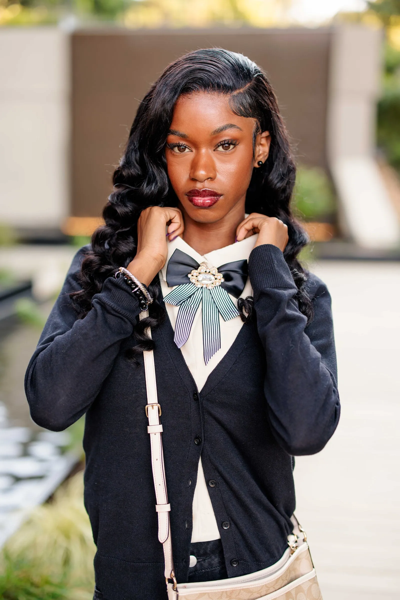 A senior adjusting her striped bow brooch, long curls over a navy cardigan.