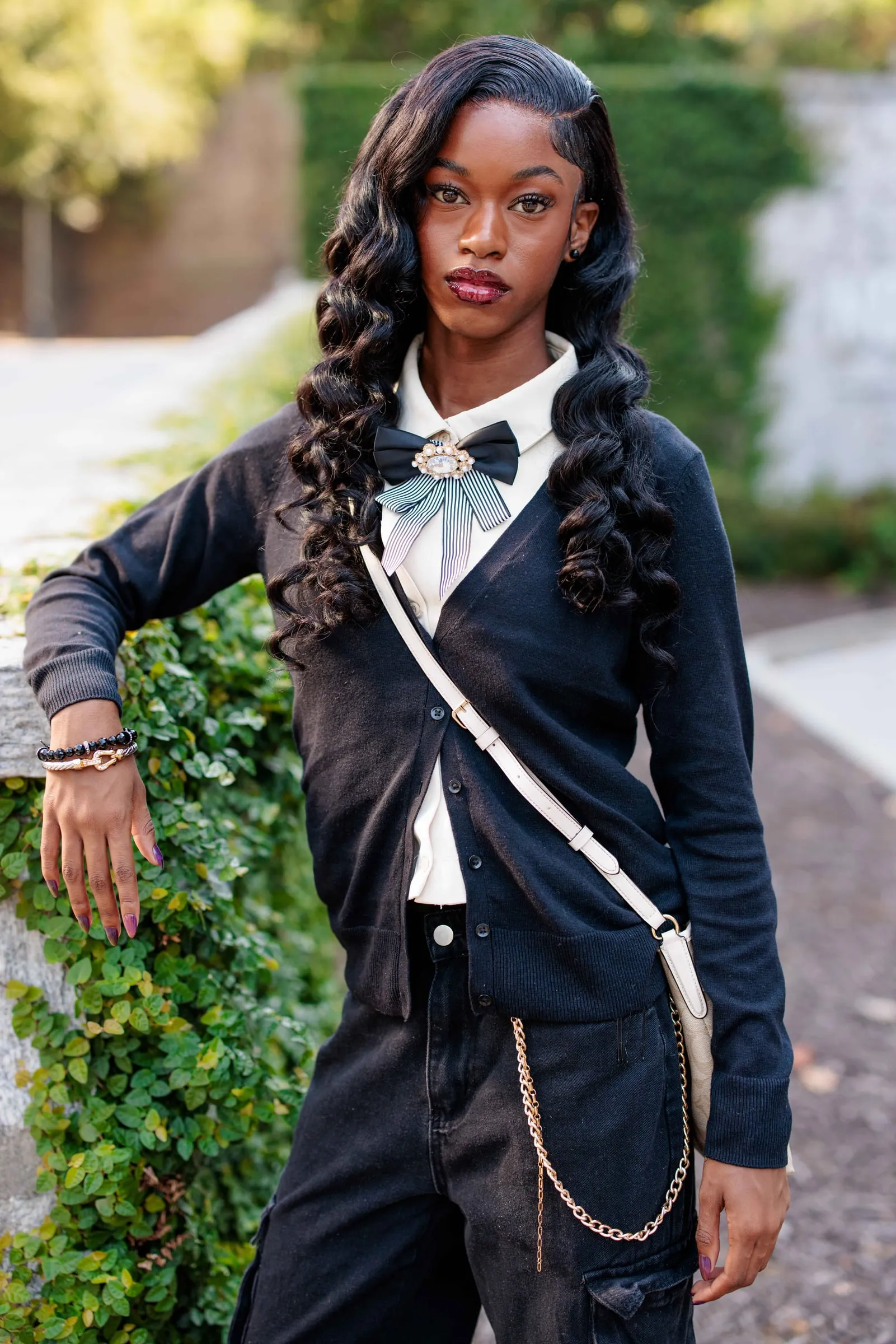 A senior in a navy cardigan and striped bow brooch posing before an ivy-covered wall.