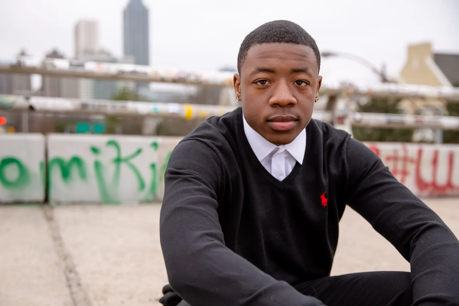 A senior in a black polo seated on a wall, the downtown Atlanta skyline behind him.