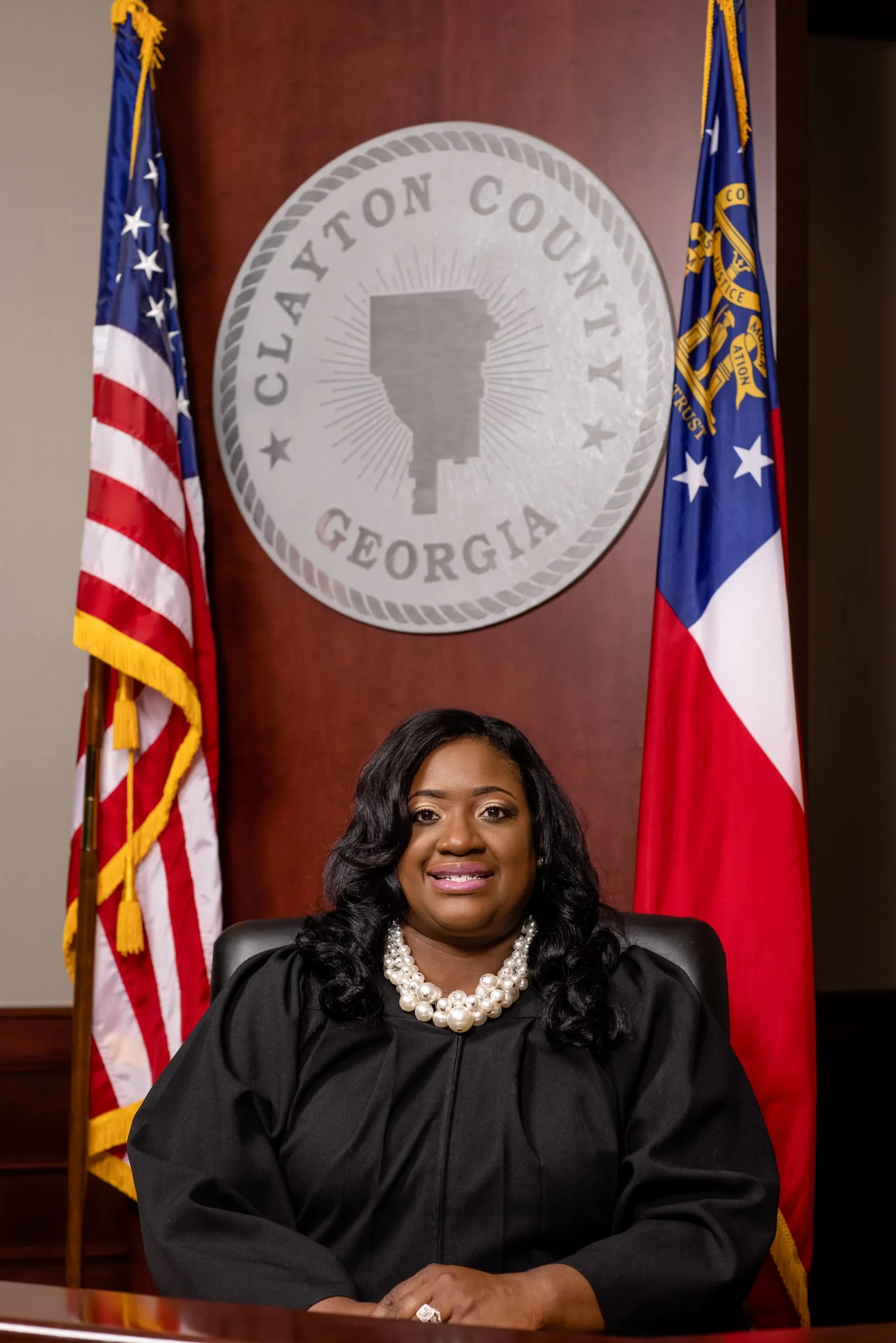 A judge in her robe seated before the Clayton County seal between two flags.