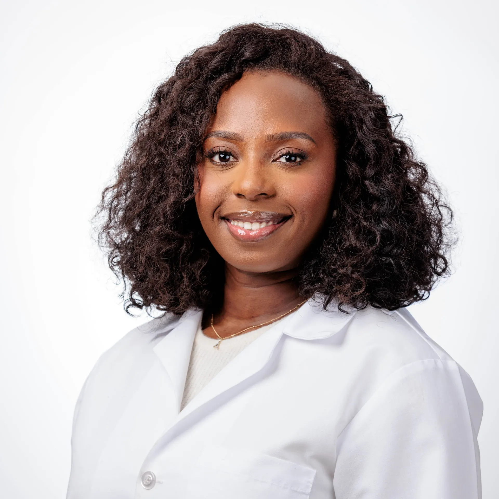 A physician in a white coat with long curls, a studio headshot on white.
