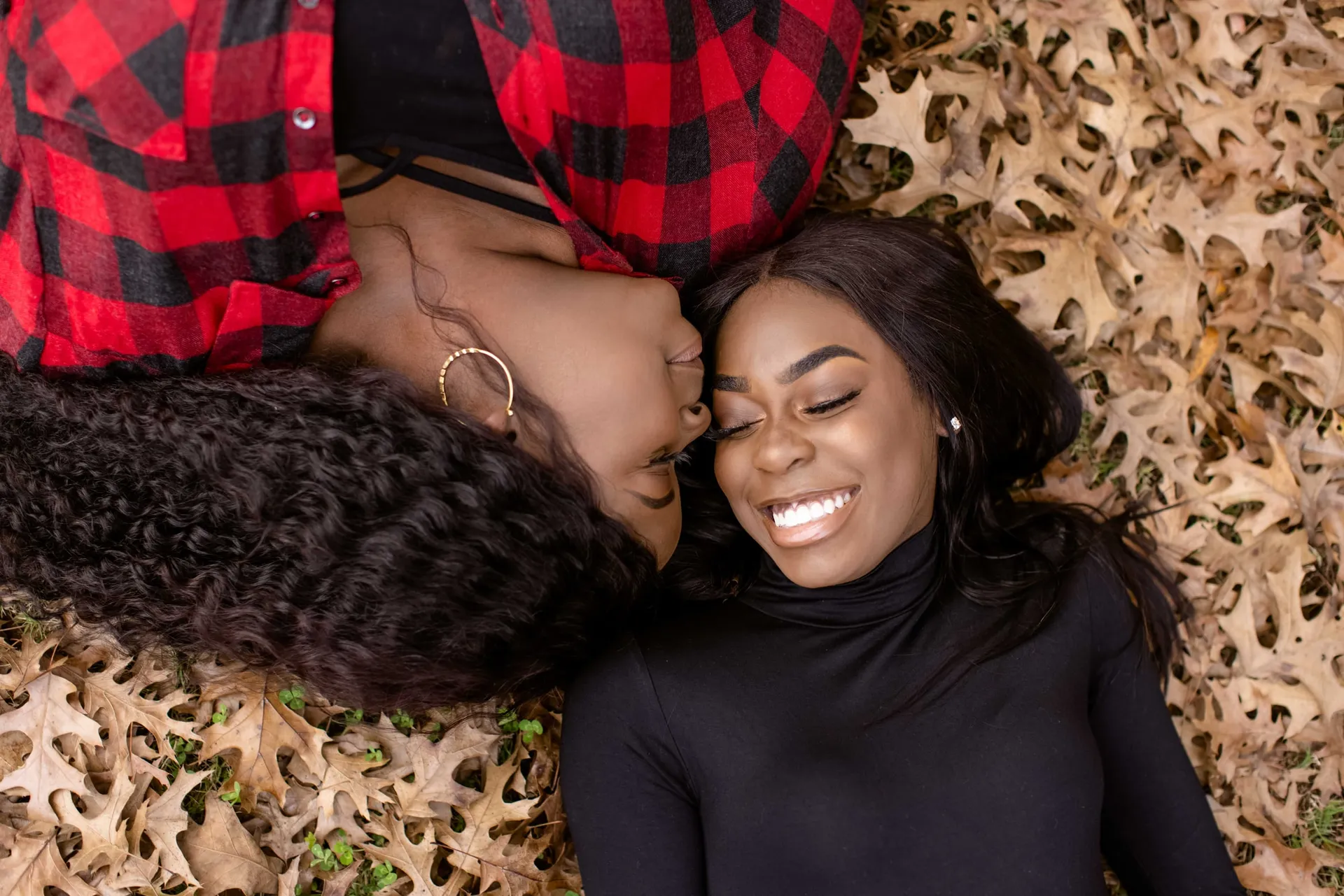 A girl in a black turtleneck lying in dry leaves, her mother's cheek on her head.