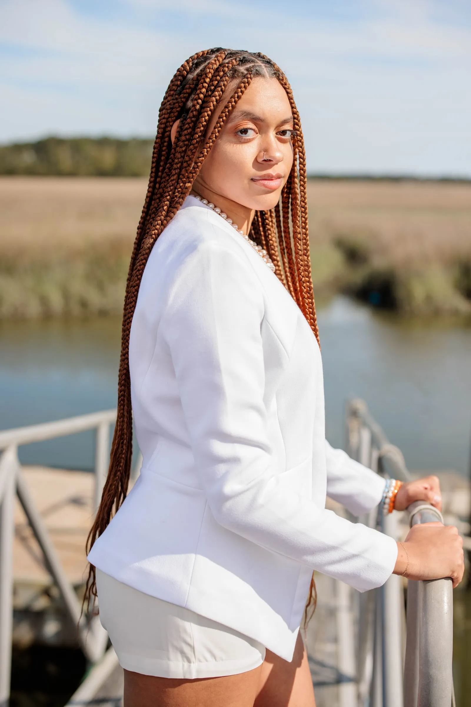 A young woman in a white blazer and shorts at a railing over a tidal marsh.