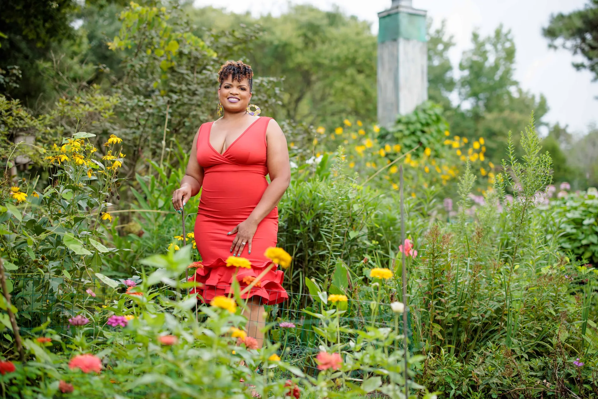 A woman in a red dress standing among zinnias and wildflowers in a summer garden.